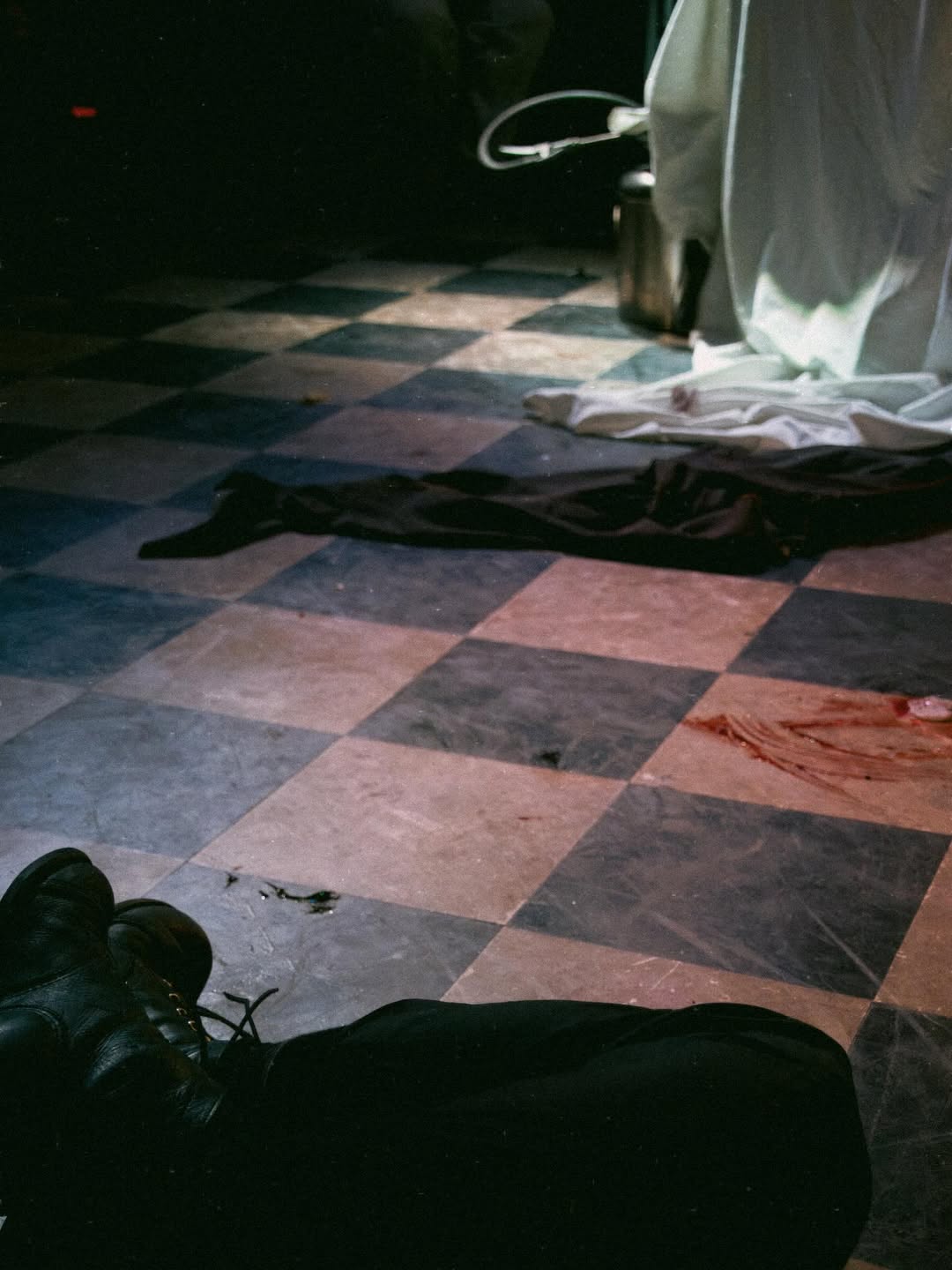 An abandoned coat lays on the floor next to a smear of blood and two lifeless legs.